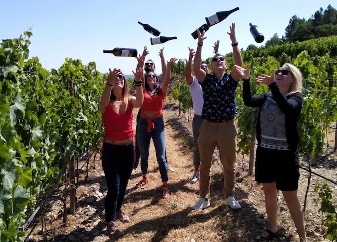 friends throwing wine bottles up air